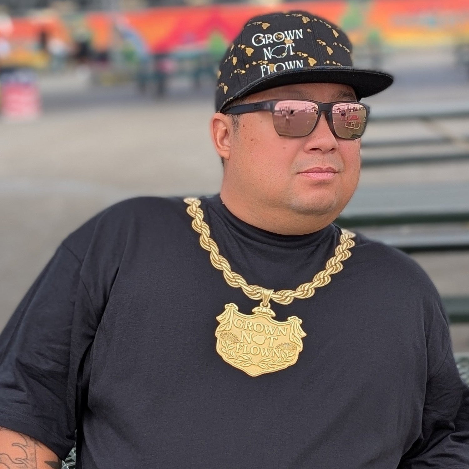 Man wearing a black crew neck, gold chain necklace print, and sunglasses with a blurred background